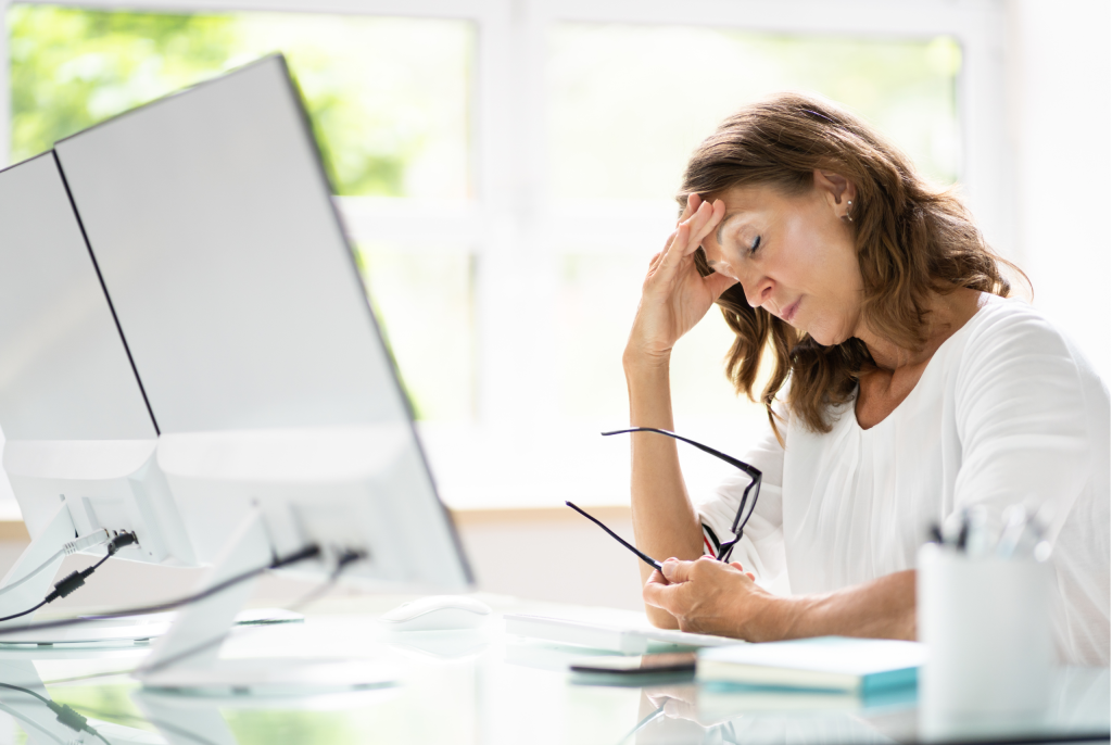 white female woman with her hand on her head holding her glasses in front of her desktop looking distressed