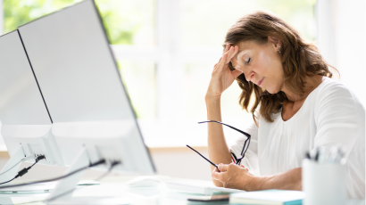 white female woman with her hand on her head holding her glasses in front of her desktop looking distressed