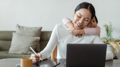 a mom with her child hugging her from behind while she is working on the laptop
