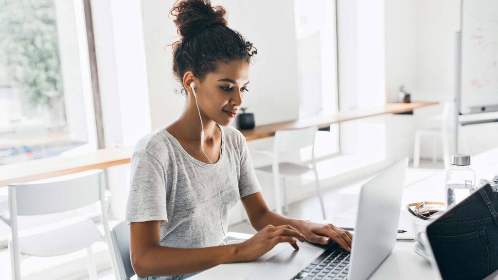 African-American young woman with white earbuds typing away on her laptop