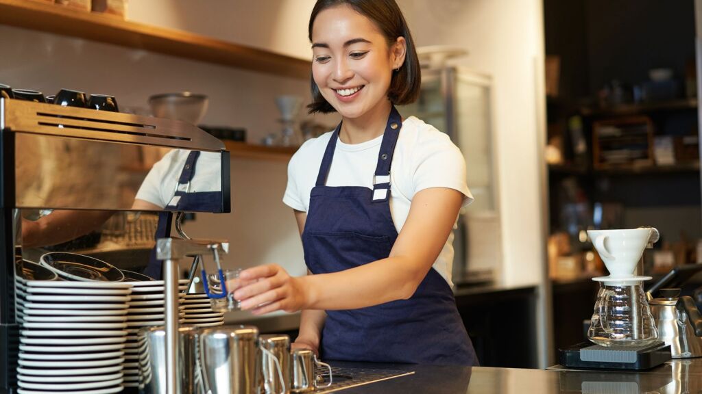 A barista smiling as she works an early shift behind a coffee counter